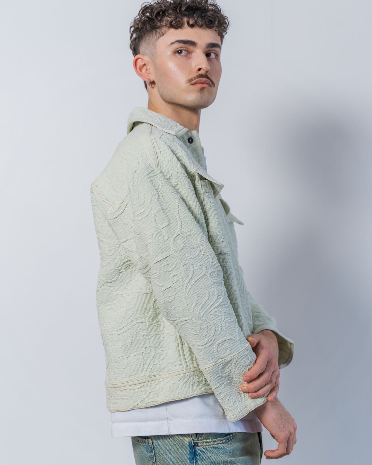 Man wearing a light green sage textured jacket against a plain background. The jacket is made from sustainable upcycled vintage textiles