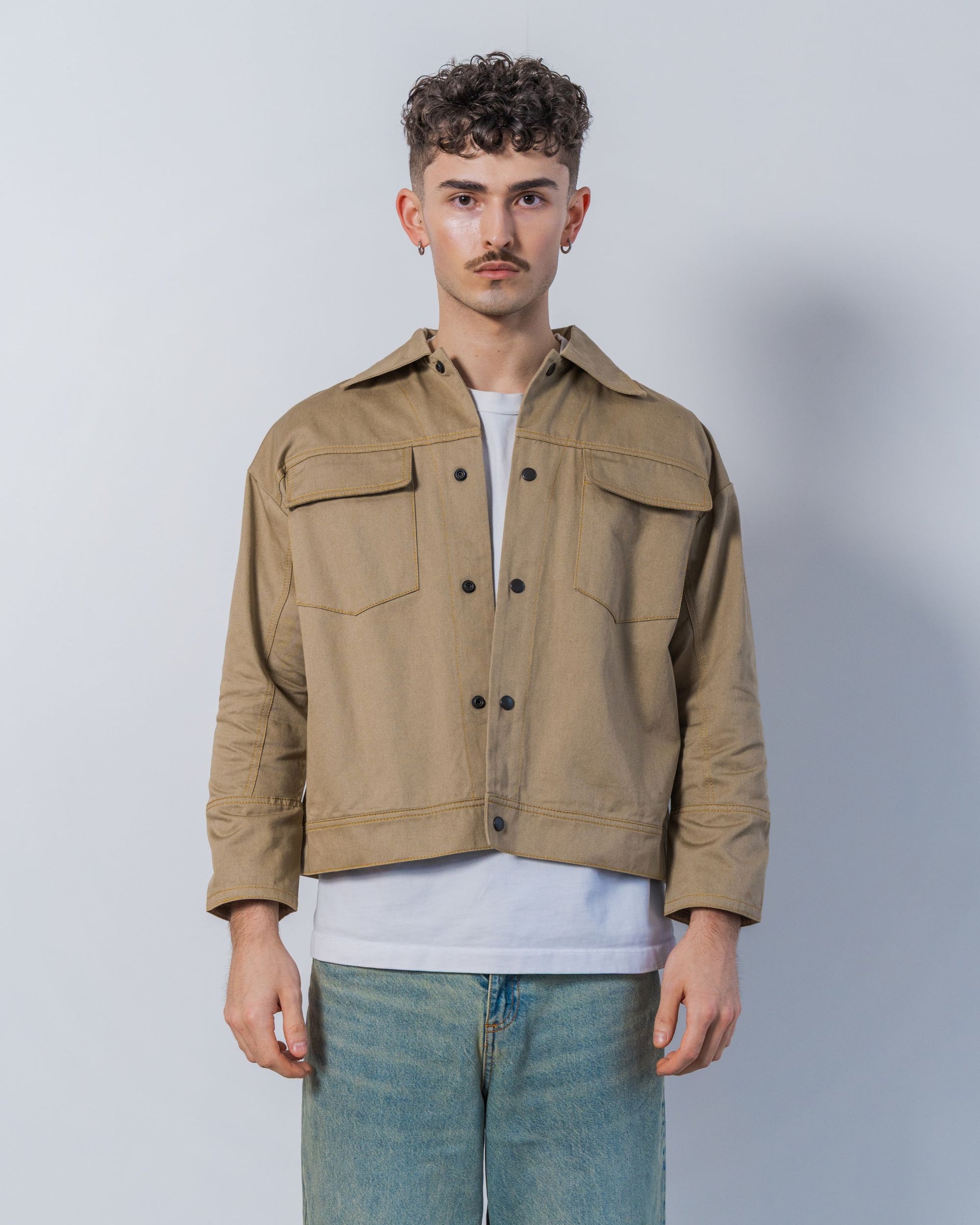 Man wearing a twill weave camel jacket over a white shirt with a plain background.