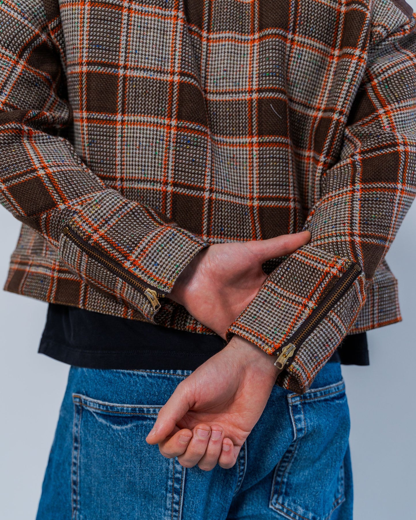 Close up on the back details of the jacket made from sustainable upcycled materials. Brown wool plaid and zupper details at the cuffs.