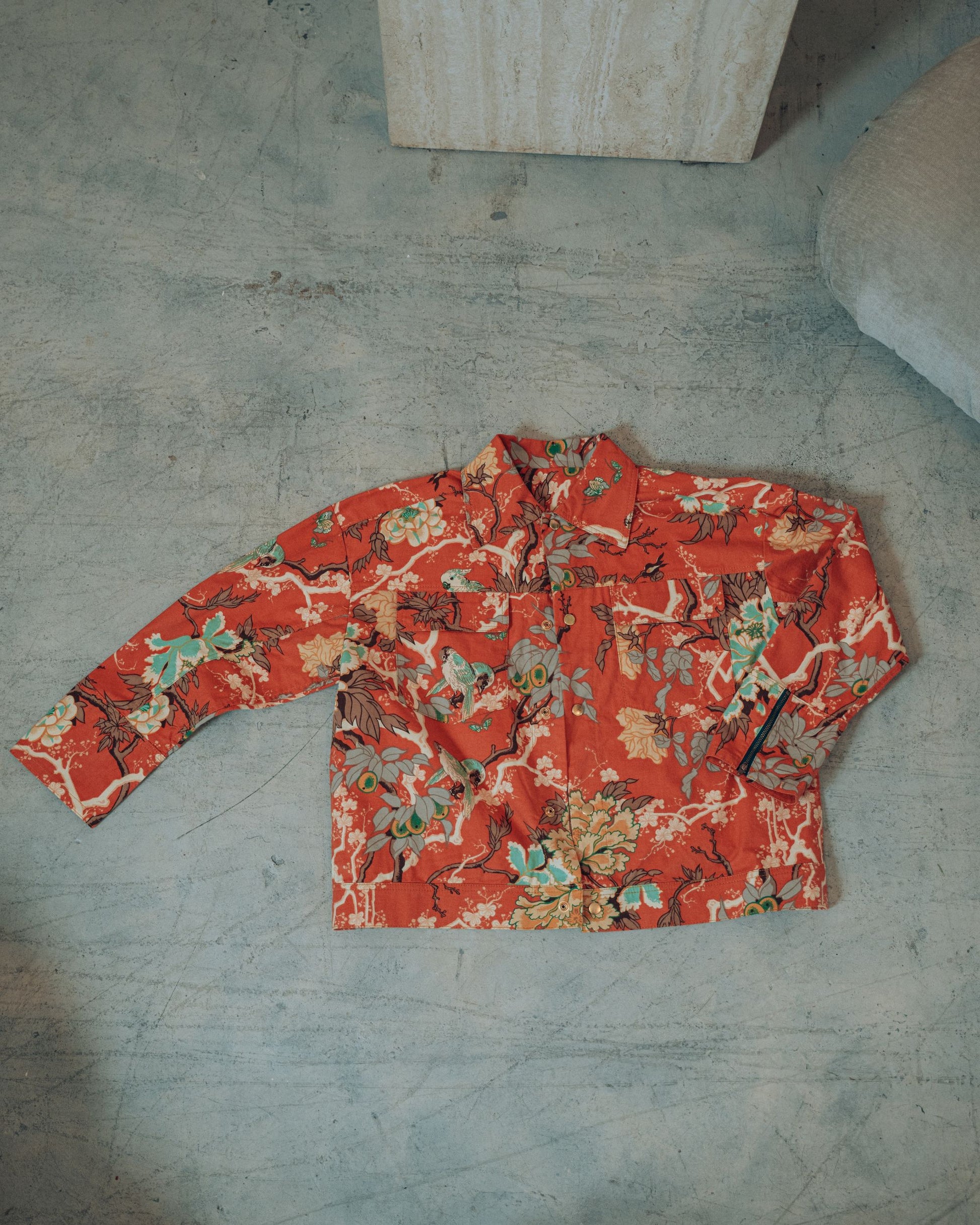 Orange jacket with floral and bird print pattern on upcycled brushed cotton placed on a concrete floor