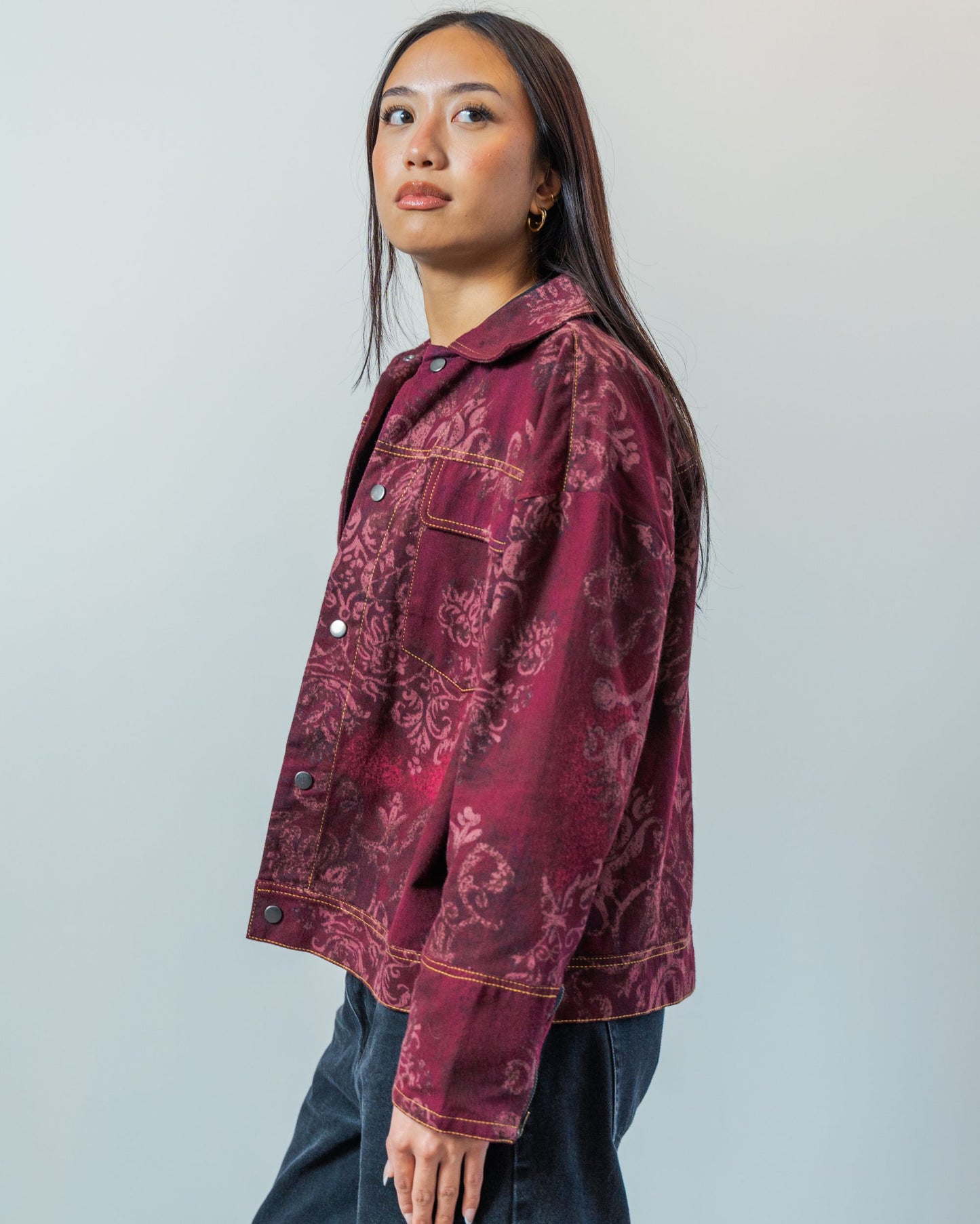 Woman wearing a burgundy red patterned jacket with gold topstitching made from sustainable upcycled materials