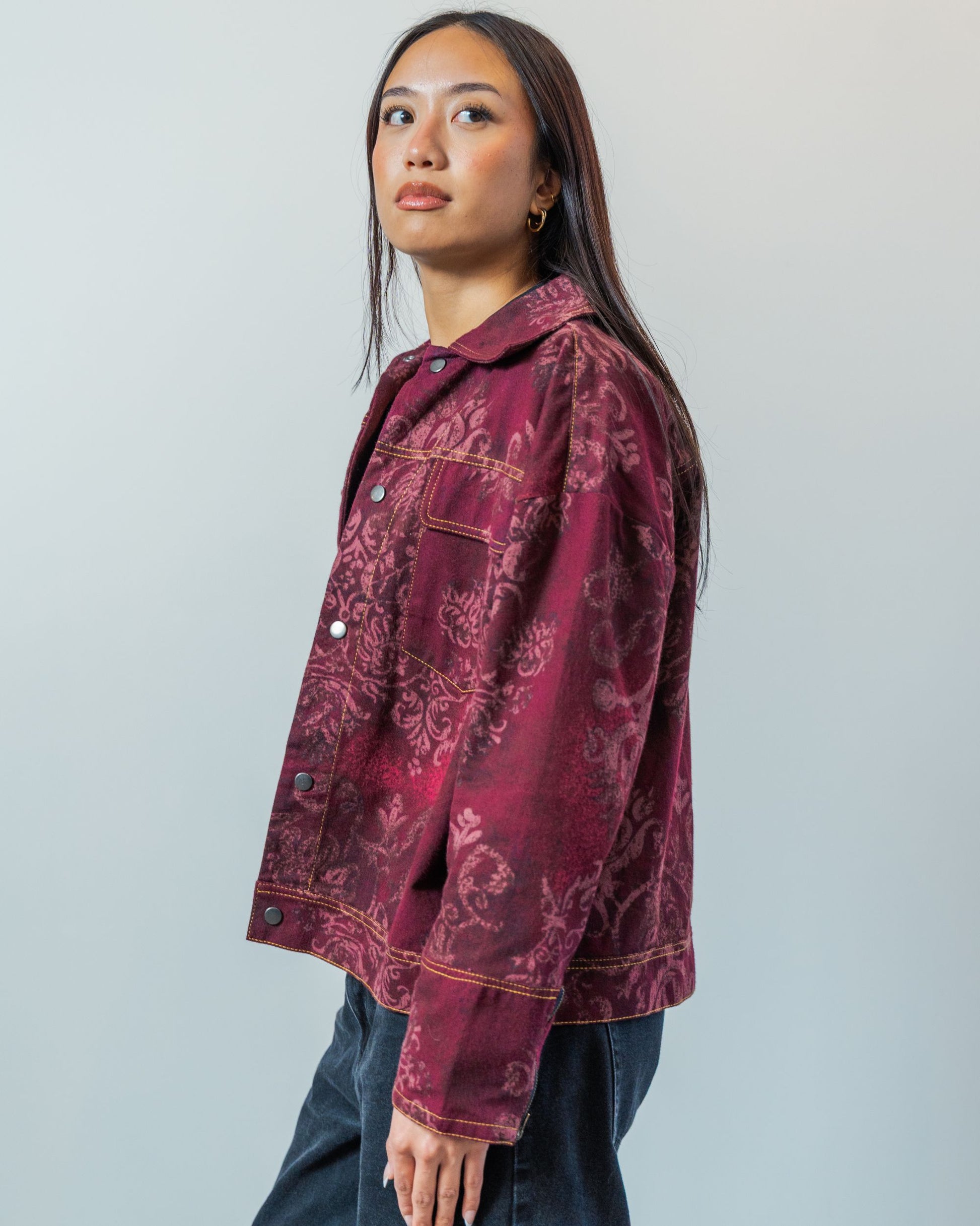 Woman wearing a burgundy red patterned jacket with gold topstitching made from sustainable upcycled materials