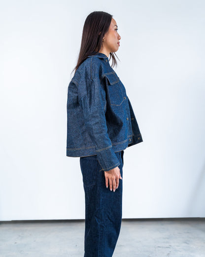 Person wearing a blue raw denim jacket and pants against a white background