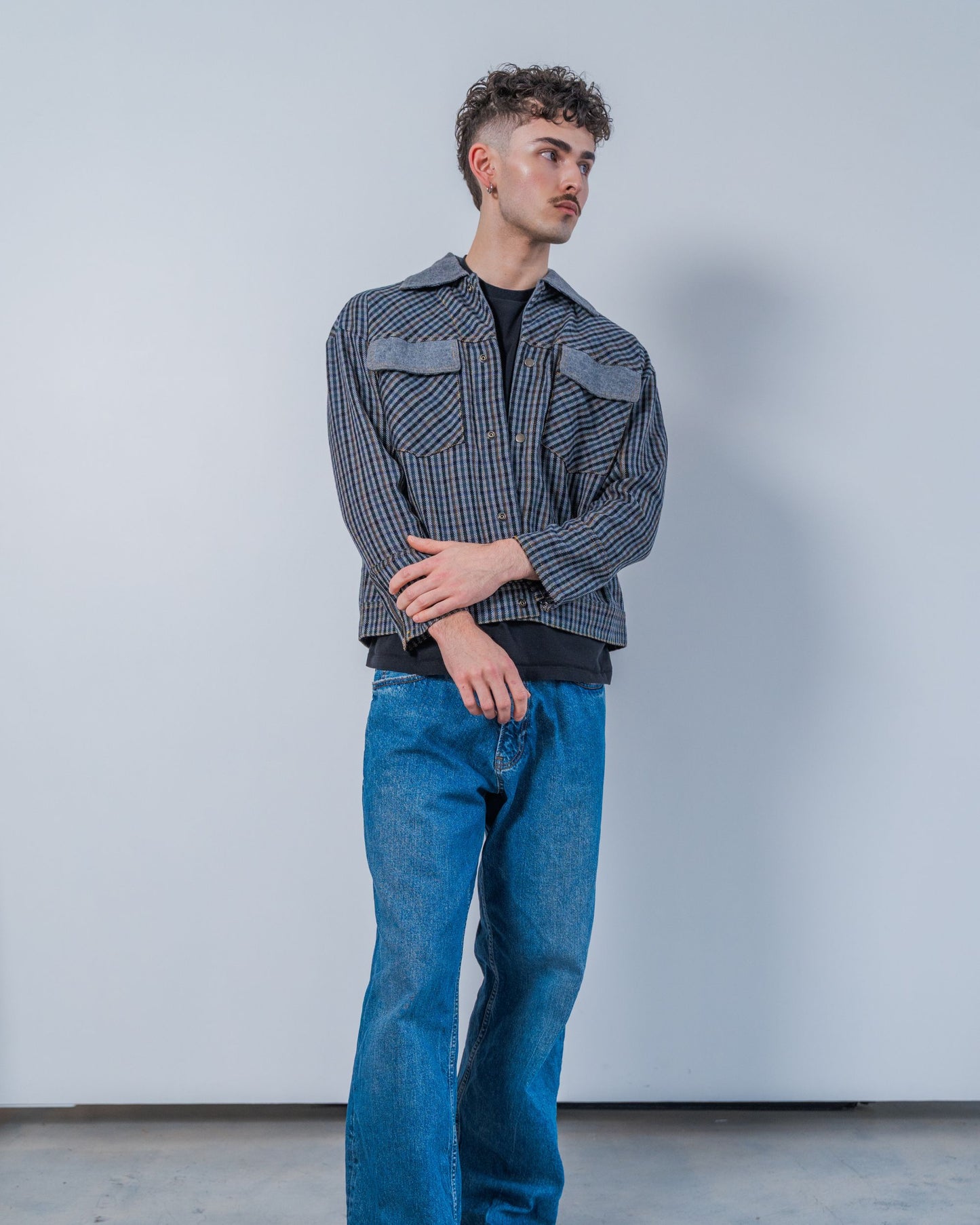 Man wearing a wool plaid jacket and jeans against a plain background. The jacket is sustainable and unisex, made from upcycled high quality wool materials.