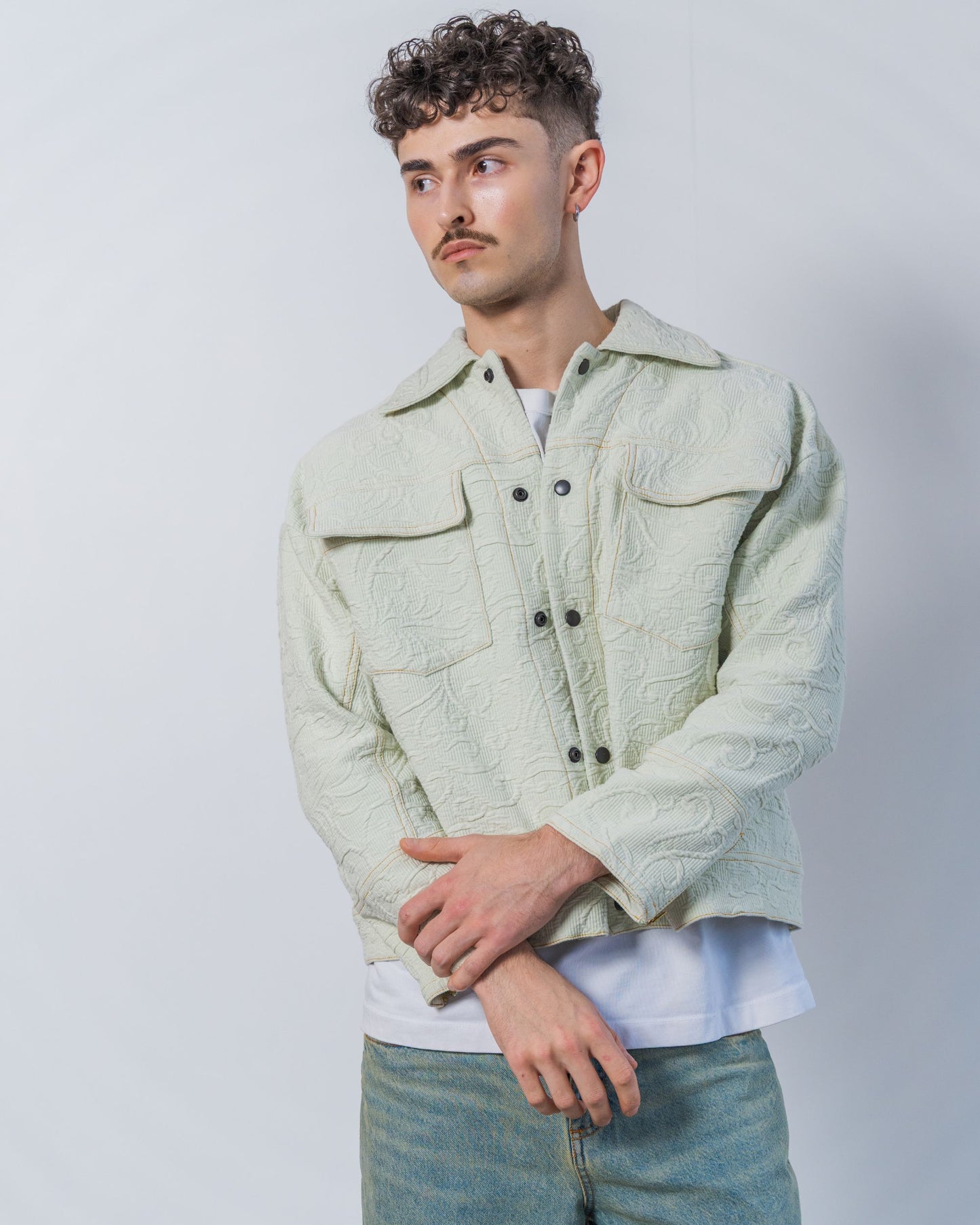 Man wearing a light green sage textured jacket against a plain background. The jacket is made from sustainable upcycled vintage textiles