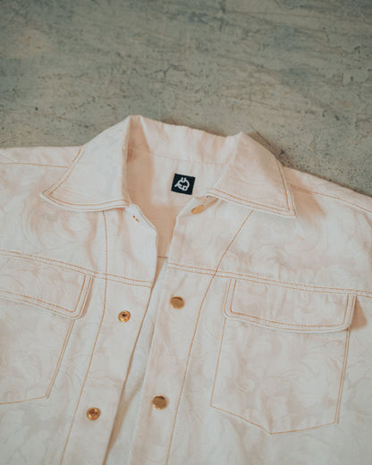 Cream jacquard print jacket with gold buttons and top stitching on a blurred background