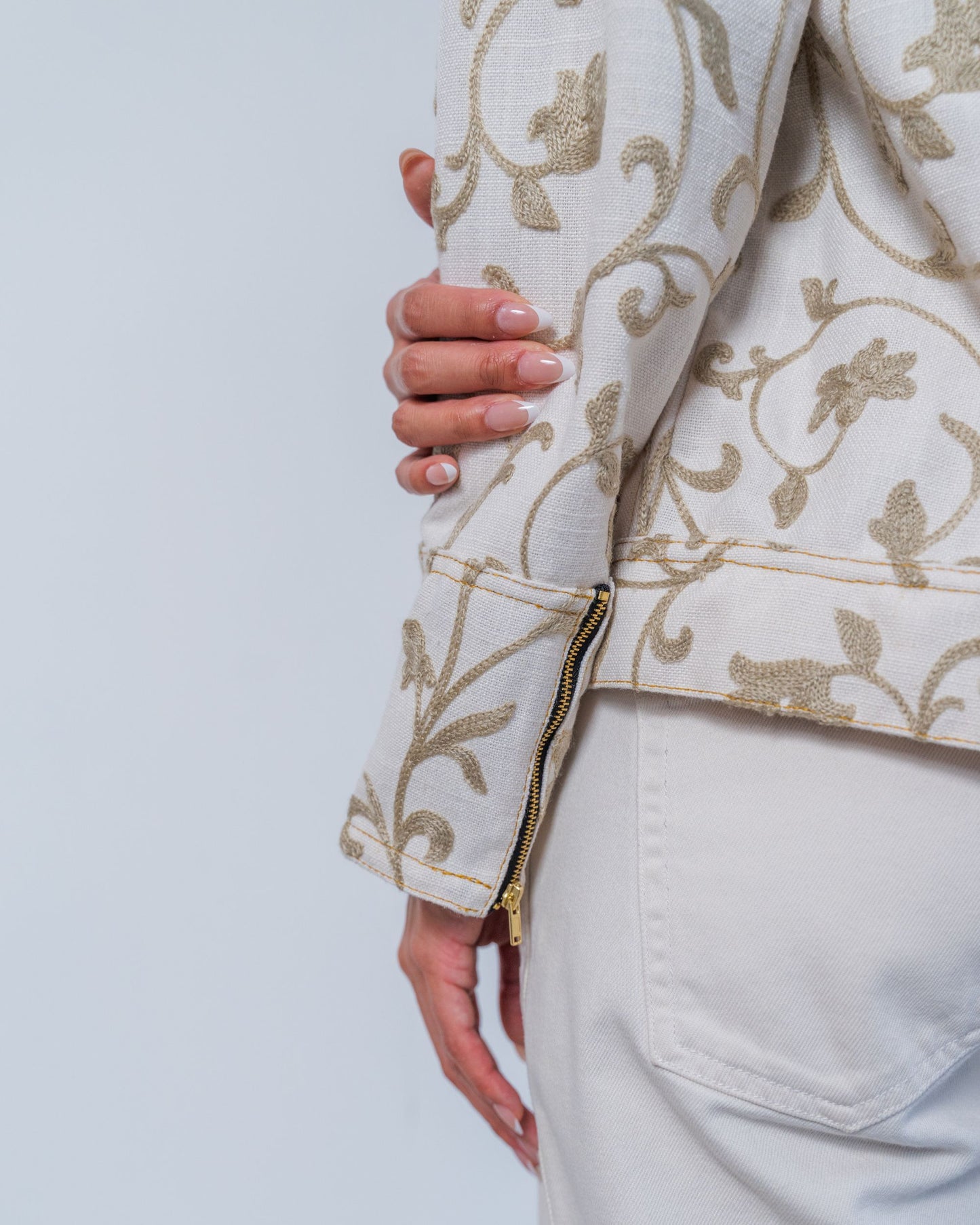 Close-up on white jacket with grey  floral embroidery and gold zippers on a plain background