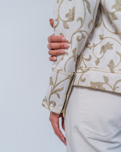 Close-up on white jacket with grey  floral embroidery and gold zippers on a plain background