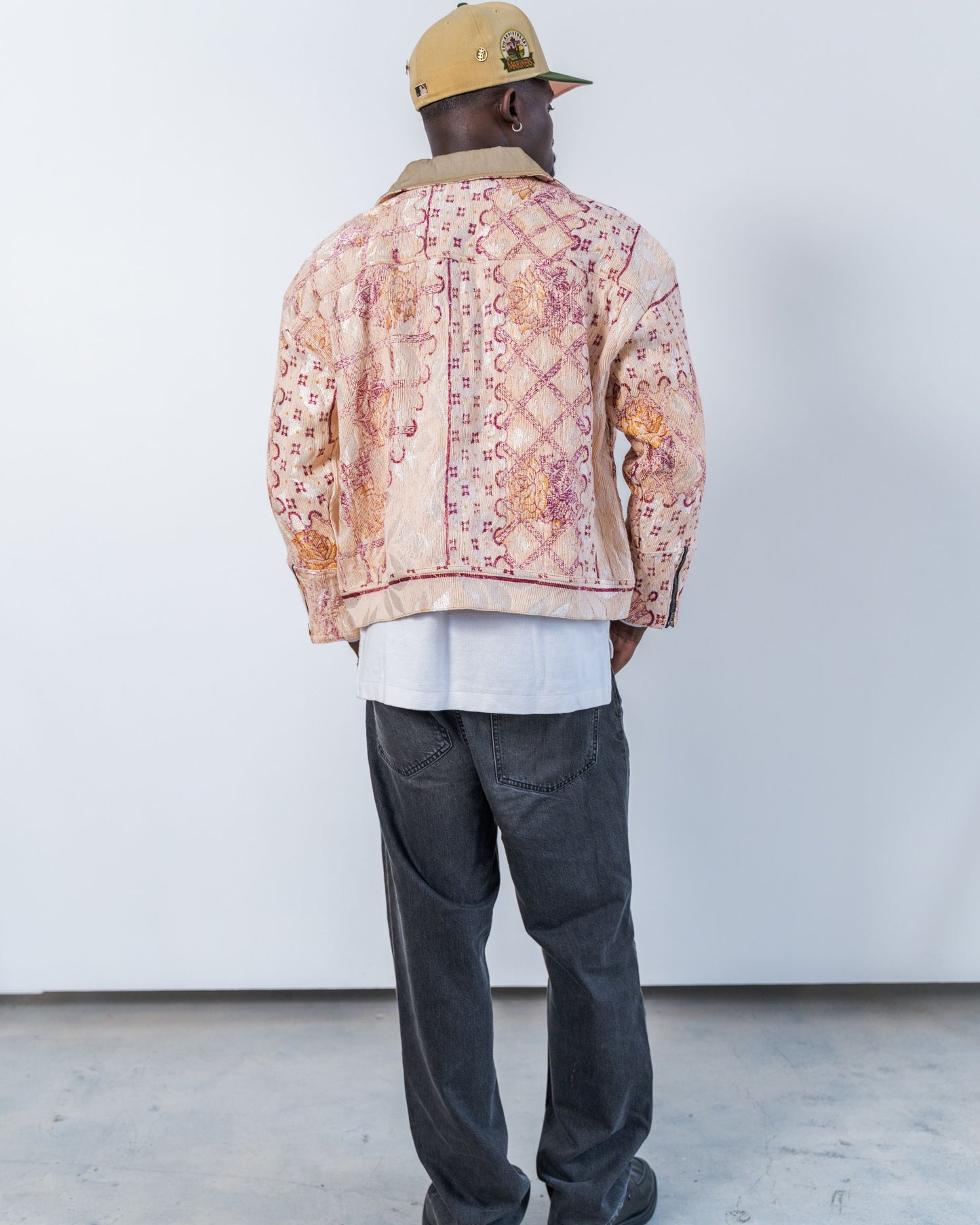 Person wearing a patterned jacket made from sustainable upcycled fabric. He is wearing a cap, standing against a white wall.