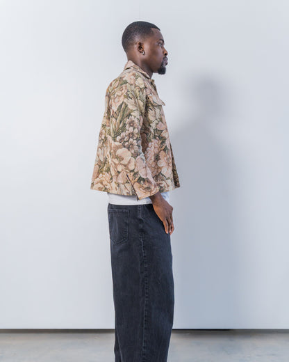 Man wearing a patterned jacket and dark jeans against a plain background. The jacket is pink and brown with a jacquard floral print. It is sustainable and unisex. 