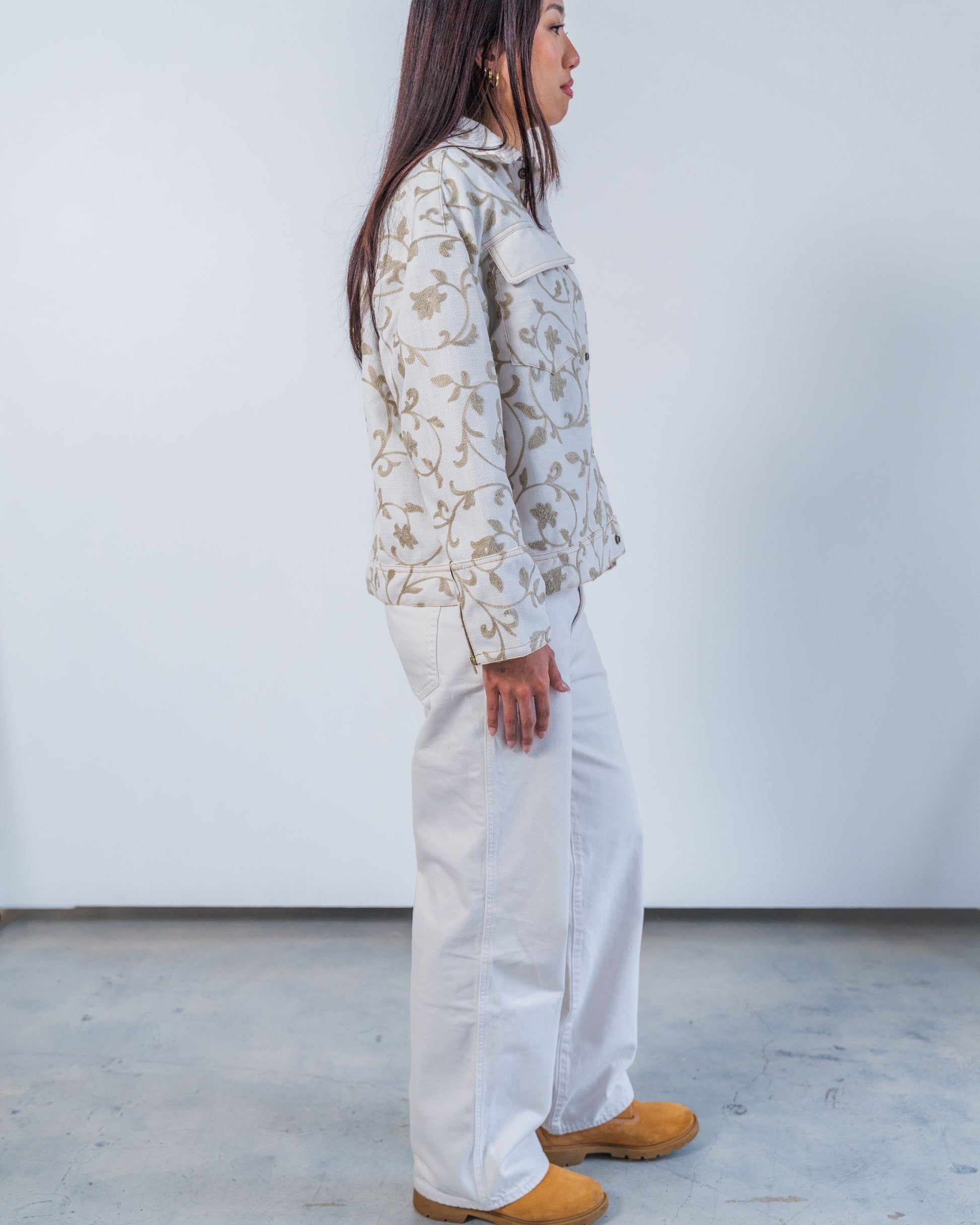 Woman wearing unisex upcycled white jacket with grey floral embroidery on a plain background