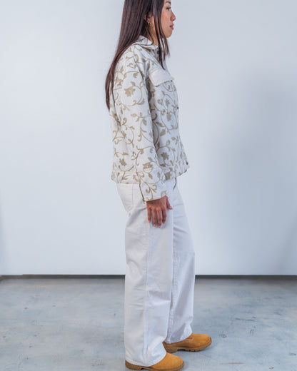 Woman wearing unisex upcycled white jacket with grey floral embroidery on a plain background