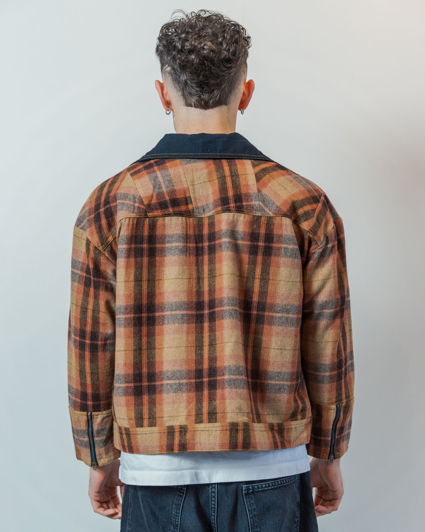 Person wearing a brown plaid jacket with a neutral background. THe jacket is made from sustainable upcycled wool fabric.