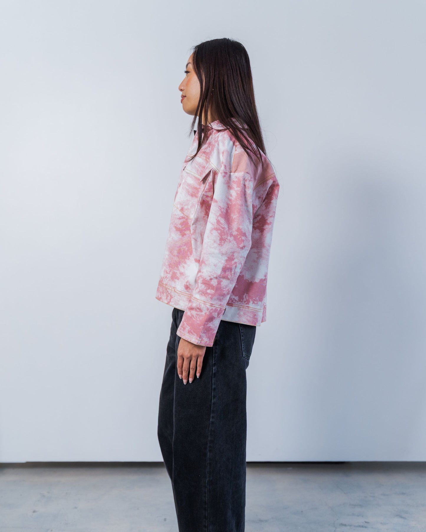 Person wearing a pink tie-dye shirt and dark pants against a white background