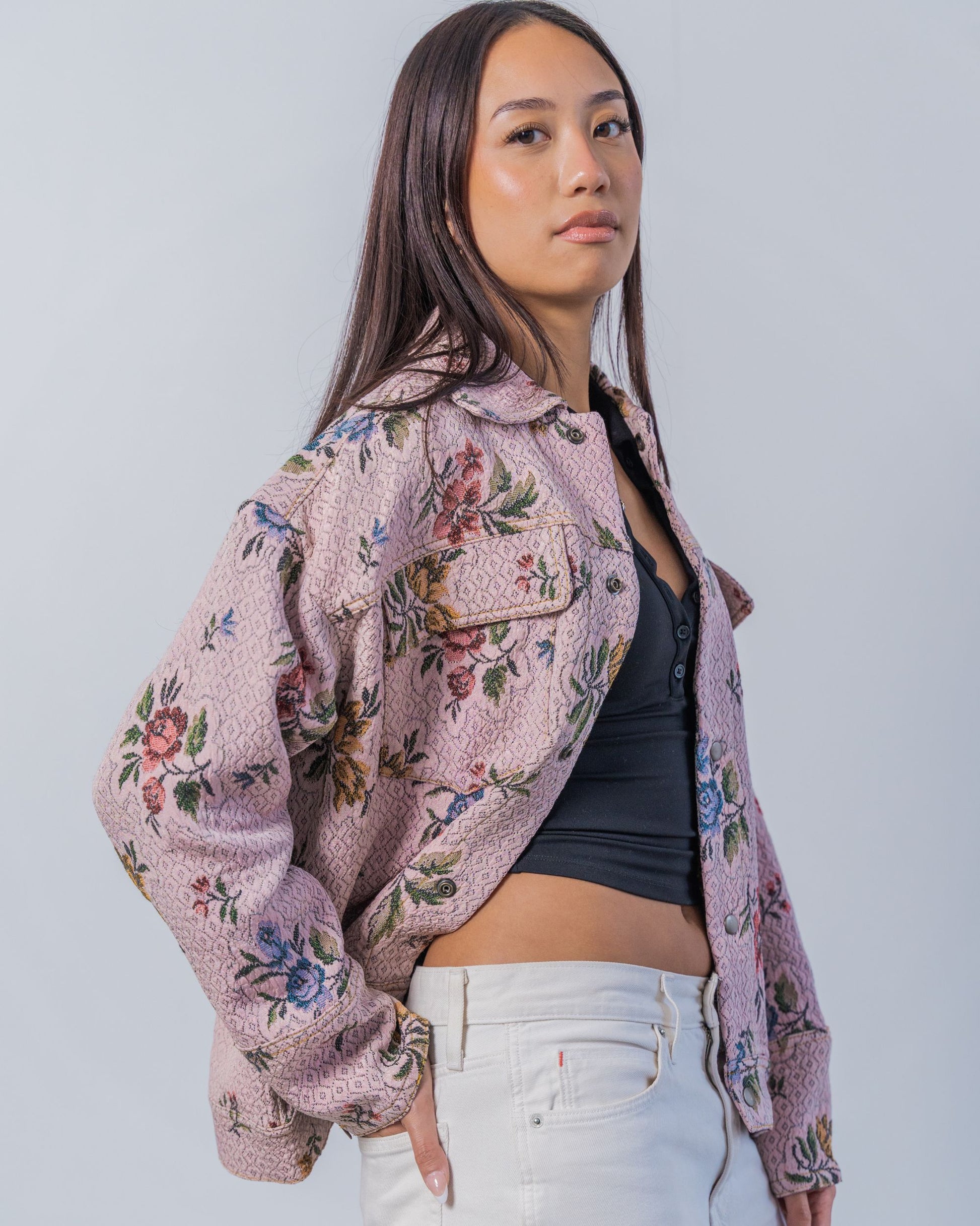 Woman wearing a floral patterned jacket over a black top and white pants on a plain background