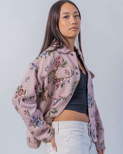 Woman wearing a floral patterned jacket over a black top and white pants on a plain background