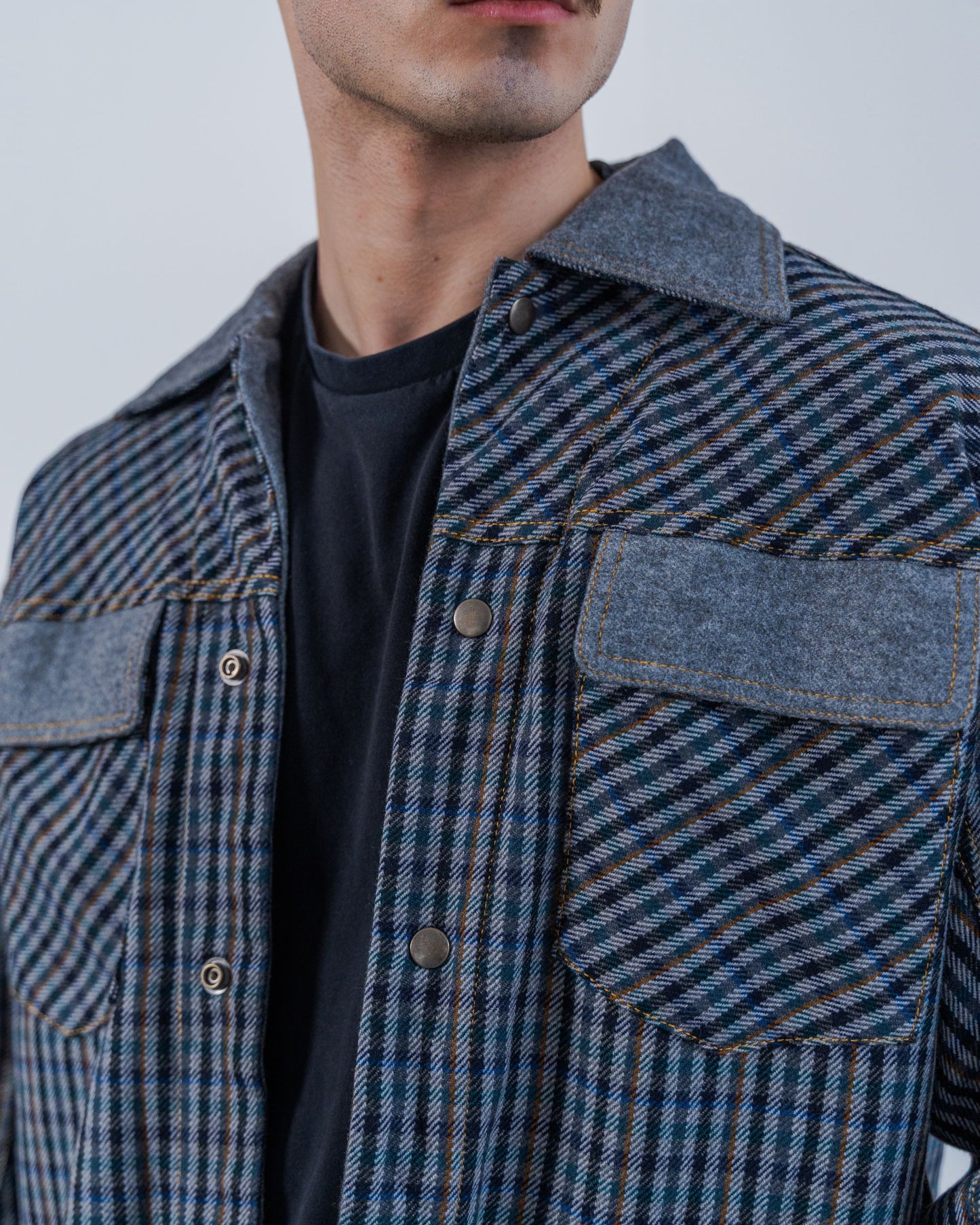 Man wearing a wool plaid jacket The jacket is sustainable and unisex, made from upcycled high quality wool materials. Close up shows the snaps and gold thread top stitching.