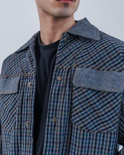 Man wearing a wool plaid jacket The jacket is sustainable and unisex, made from upcycled high quality wool materials. Close up shows the snaps and gold thread top stitching.