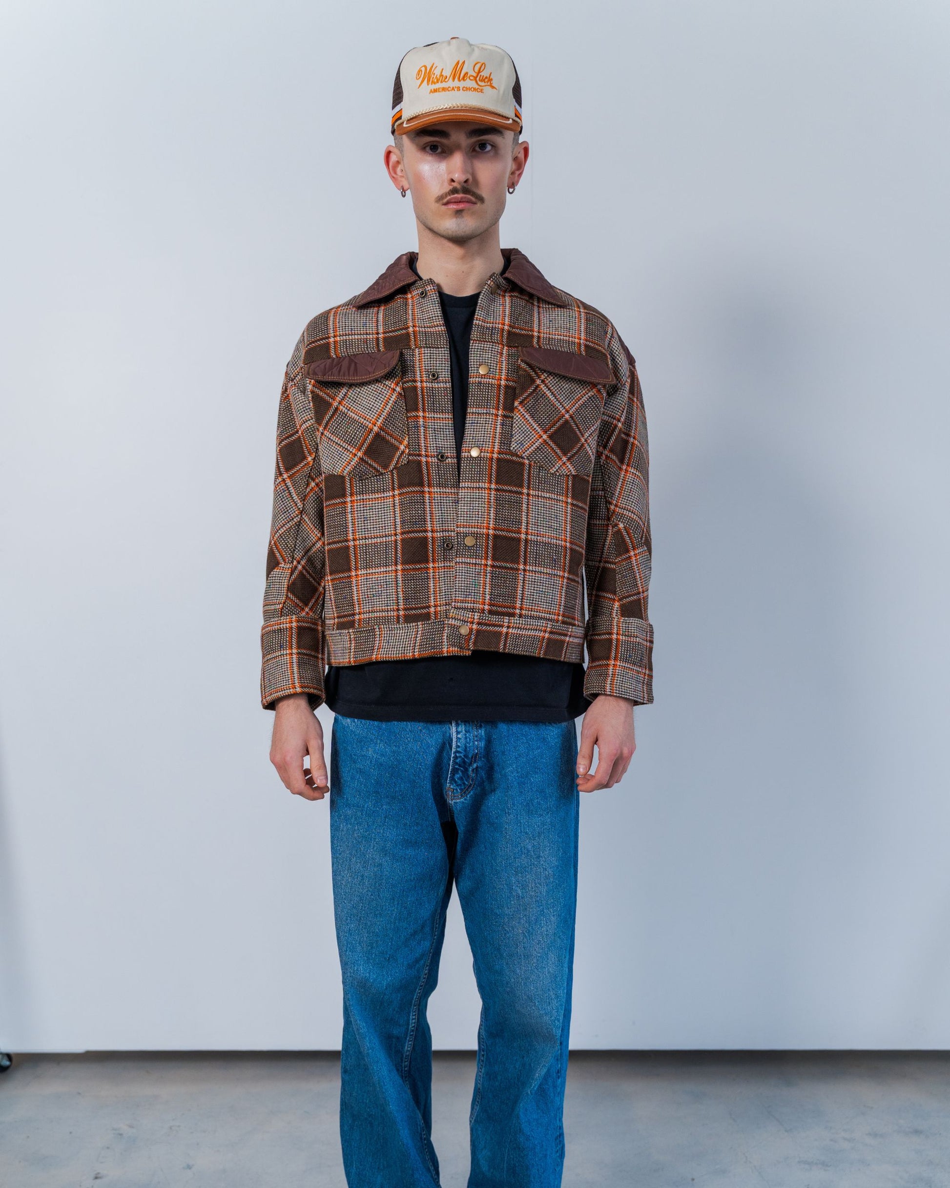 Person wearing a plaid jacket and blue jeans against a plain background. The jacket is sustainable and unisex, made from upcycled high quality wool materials. 