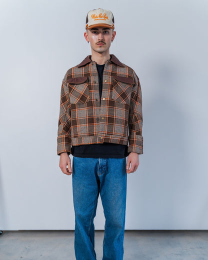 Person wearing a plaid jacket and blue jeans against a plain background. The jacket is sustainable and unisex, made from upcycled high quality wool materials. 
