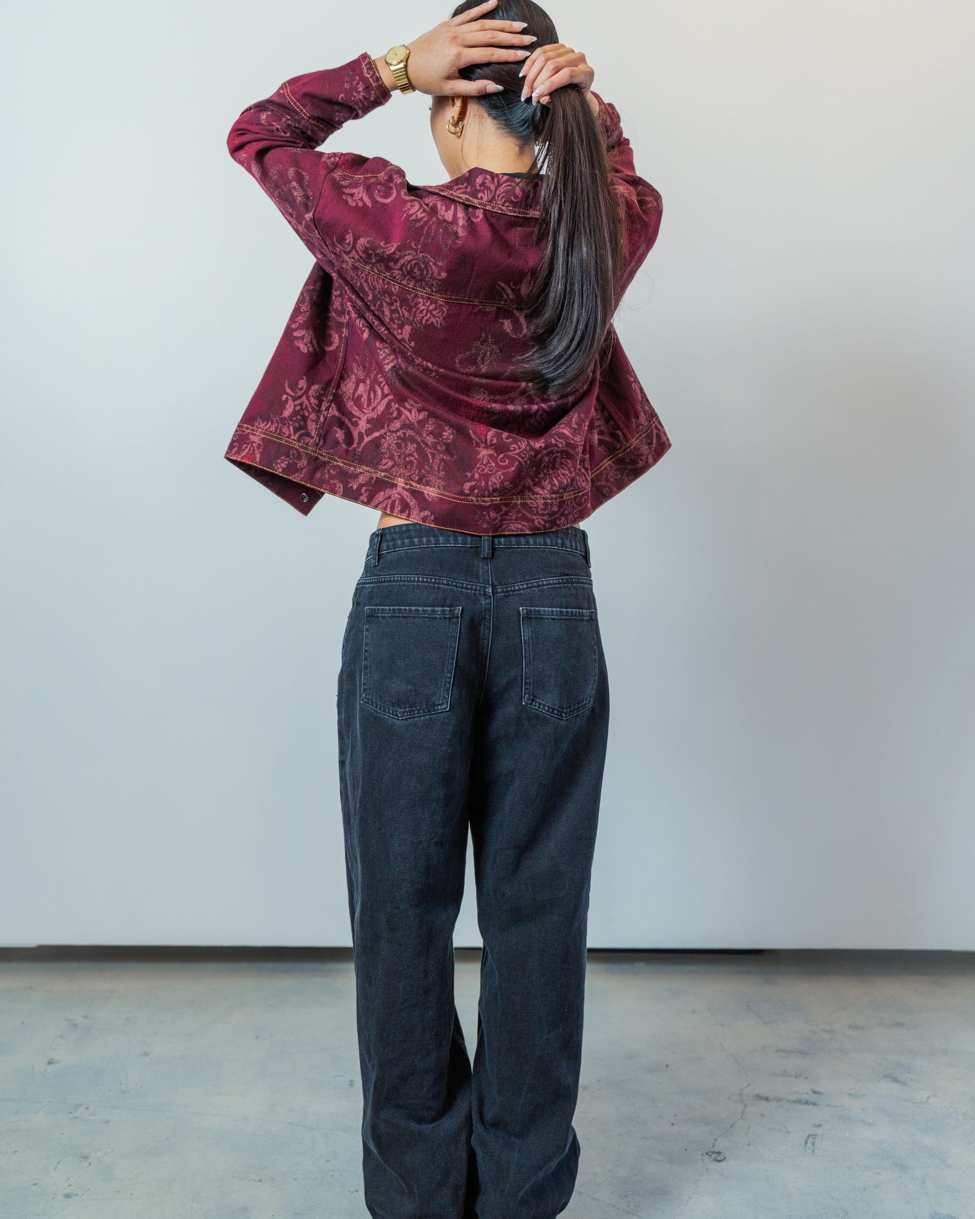 Person wearing a patterned burgundy jacket and dark jeans against a plain background