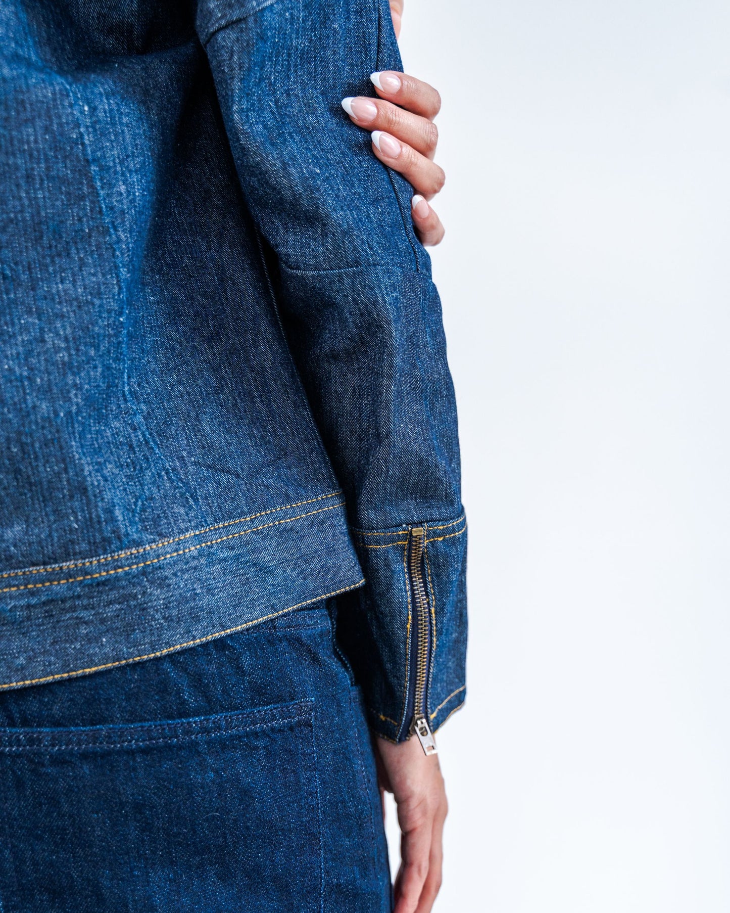 Close-up of a person wearing a blue raw denim jacket with a blurred background