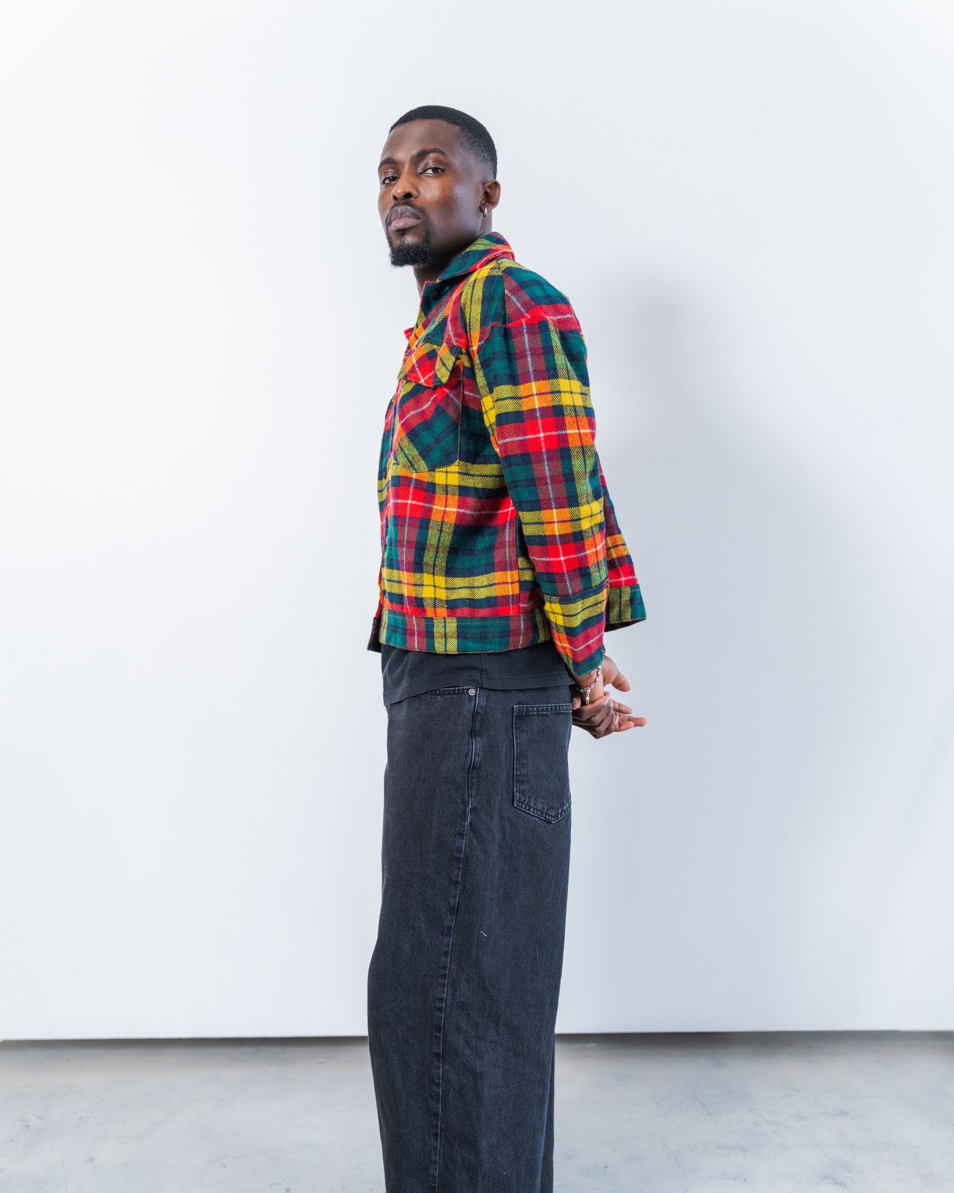 Person wearing a colorful upcycled wool plaid jacket and dark jeans against a white background
