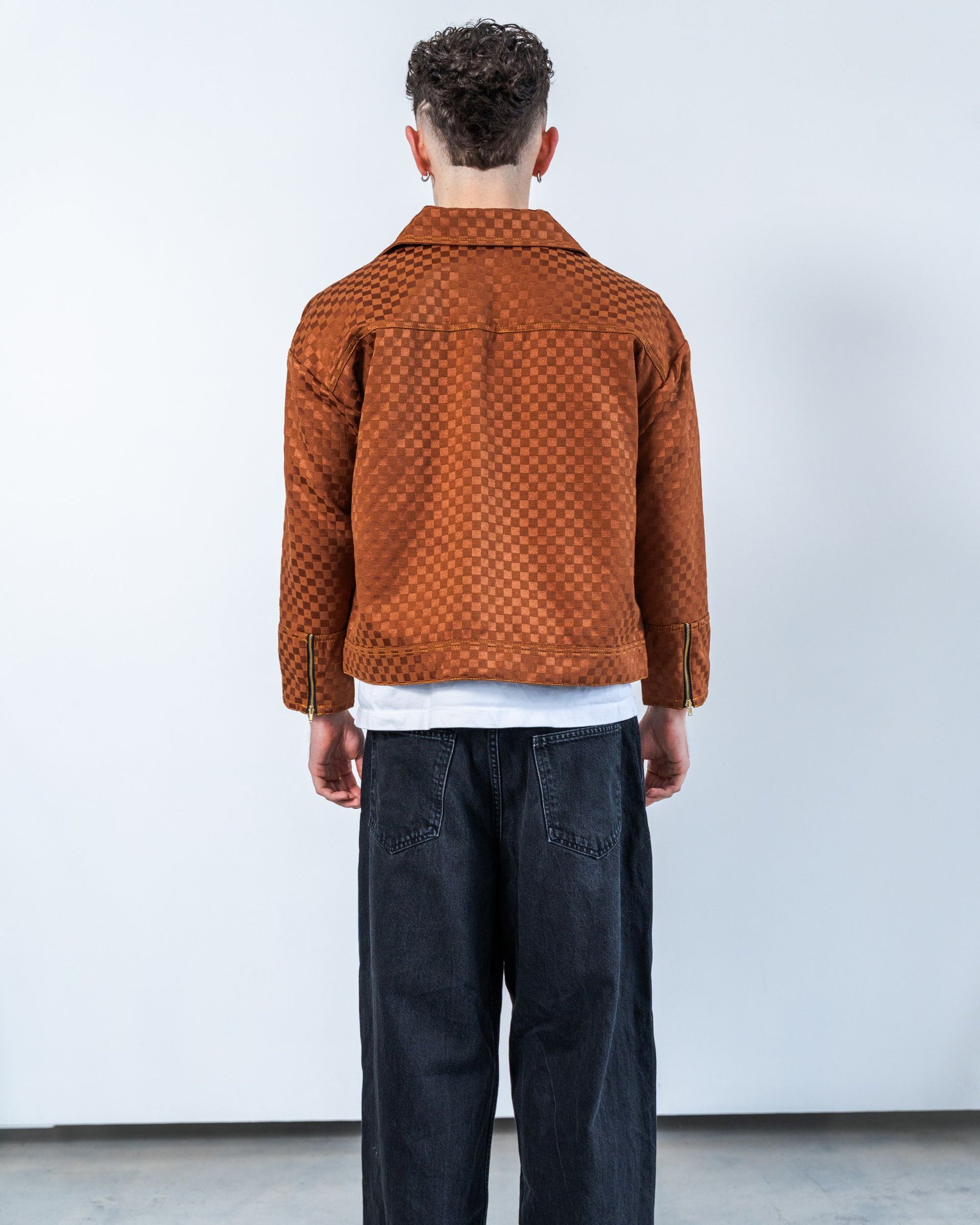 Person wearing a brown checkers patterned jacket and dark pants against a white background