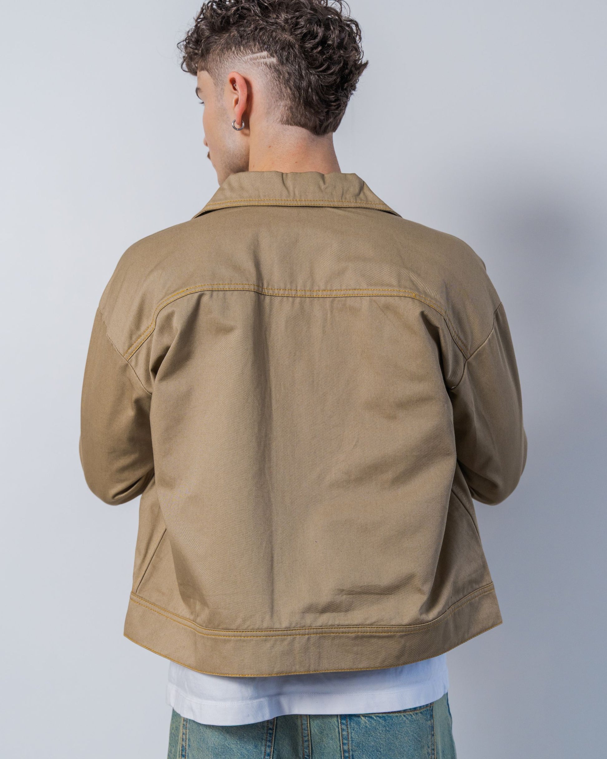 Person wearing a twill weave camel jacket against a white background. The jacket is made from sustainable upcycled materials and unisex.