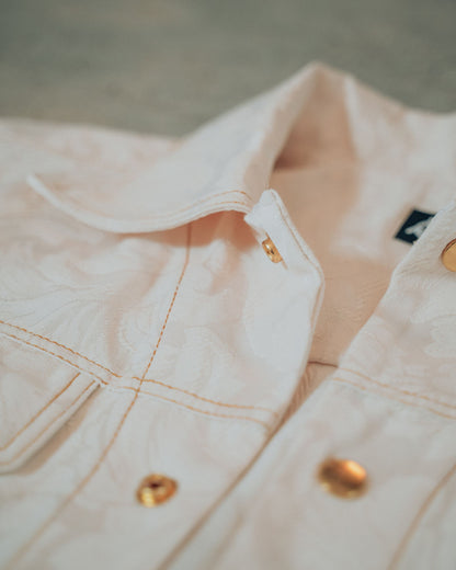 Close-up of a cream jacket with gold buttons and top stitching on a blurred background