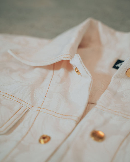 Close-up of a cream jacket with gold buttons and top stitching on a blurred background
