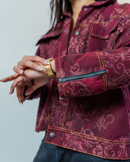 Person wearing a burgundy red patterned jacket made from sustainable upcycled materials. the jacket has zippers on the cuff and gold thread topstitching.