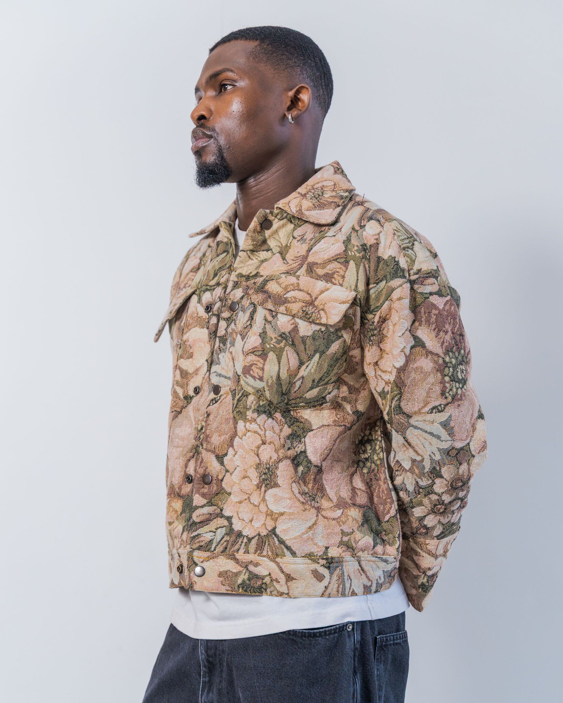 Man wearing a floral patterned jacket on a white background. The jacket is pink and brown with a jacquard floral print. It is sustainable, upcycled and unisex. 