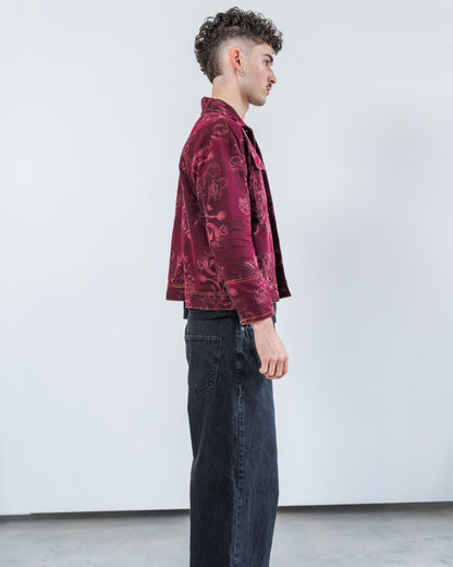 Person wearing a burgundy red patterned jacket and dark jeans against a white background