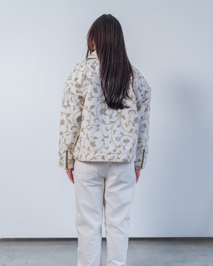 Woman wearing unisex upcycled white jacket with grey floral embroidery on a plain background