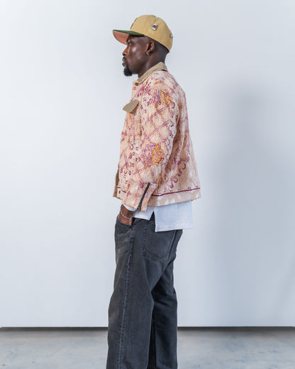 Man wearing a patterned jacket and cap against a white background. the jacket is pink with floral print made from a vintage upcycled blanket
