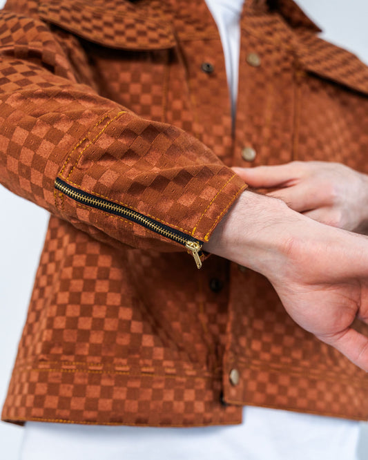 Brown checkered jacket with a close-up of a hand adjusting the sleeve. The sleeve has a zipper detail and gold top stitching.