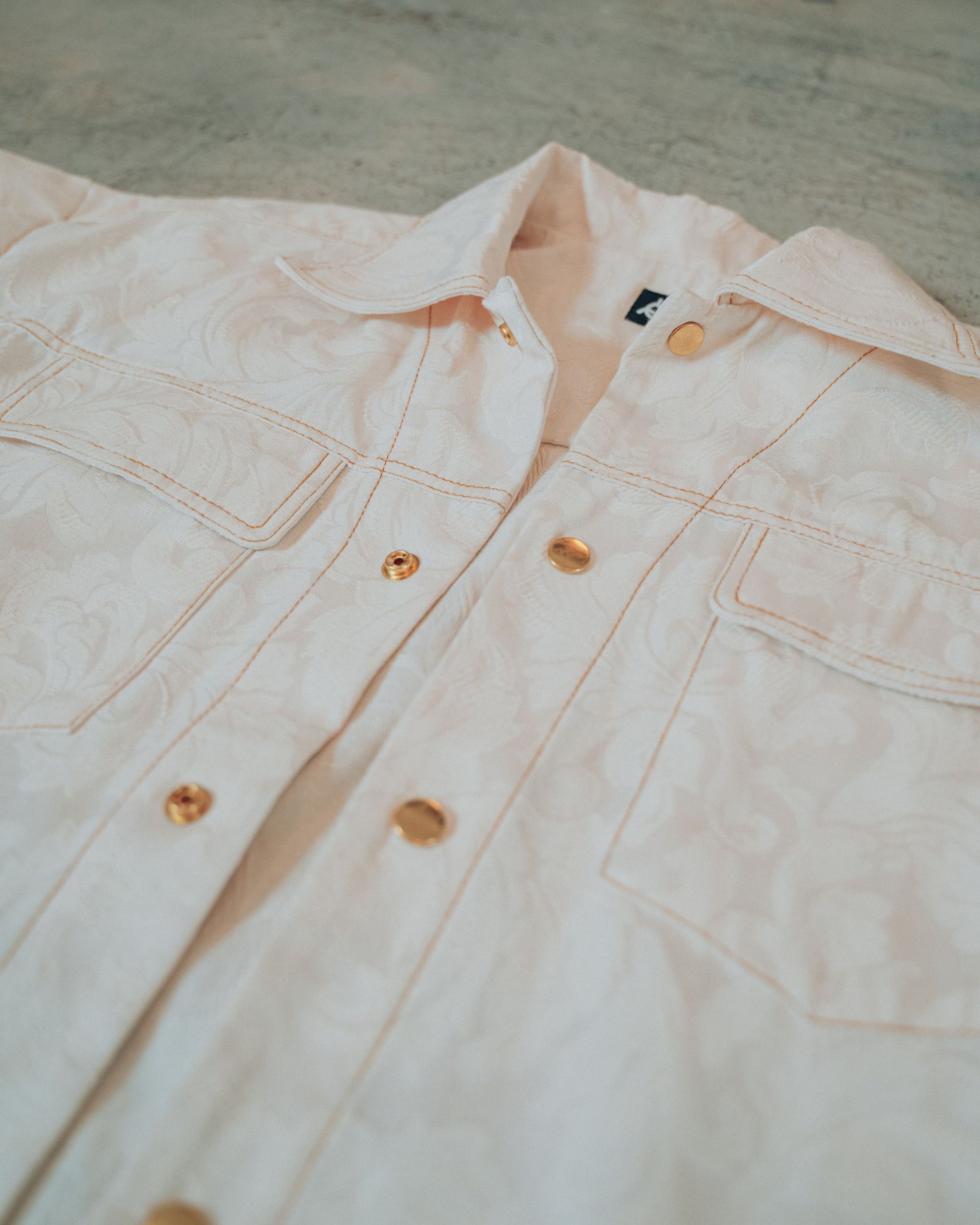 Close-up of a cream jacket with gold buttons and top stitching on a blurred background