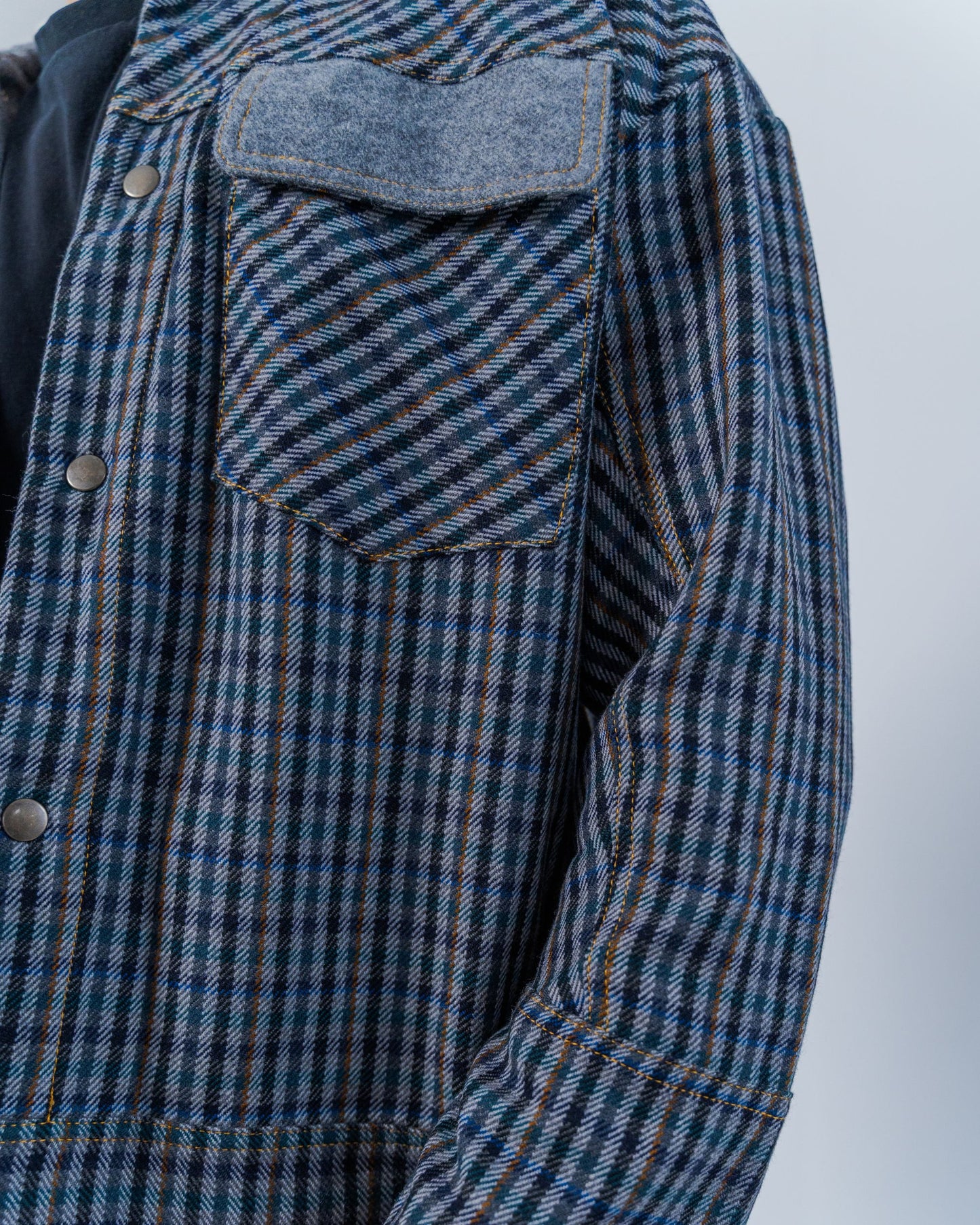 Man wearing a wool plaid jacket The jacket is sustainable and unisex, made from upcycled high quality wool materials. Close up shows the snaps and gold thread top stitching.