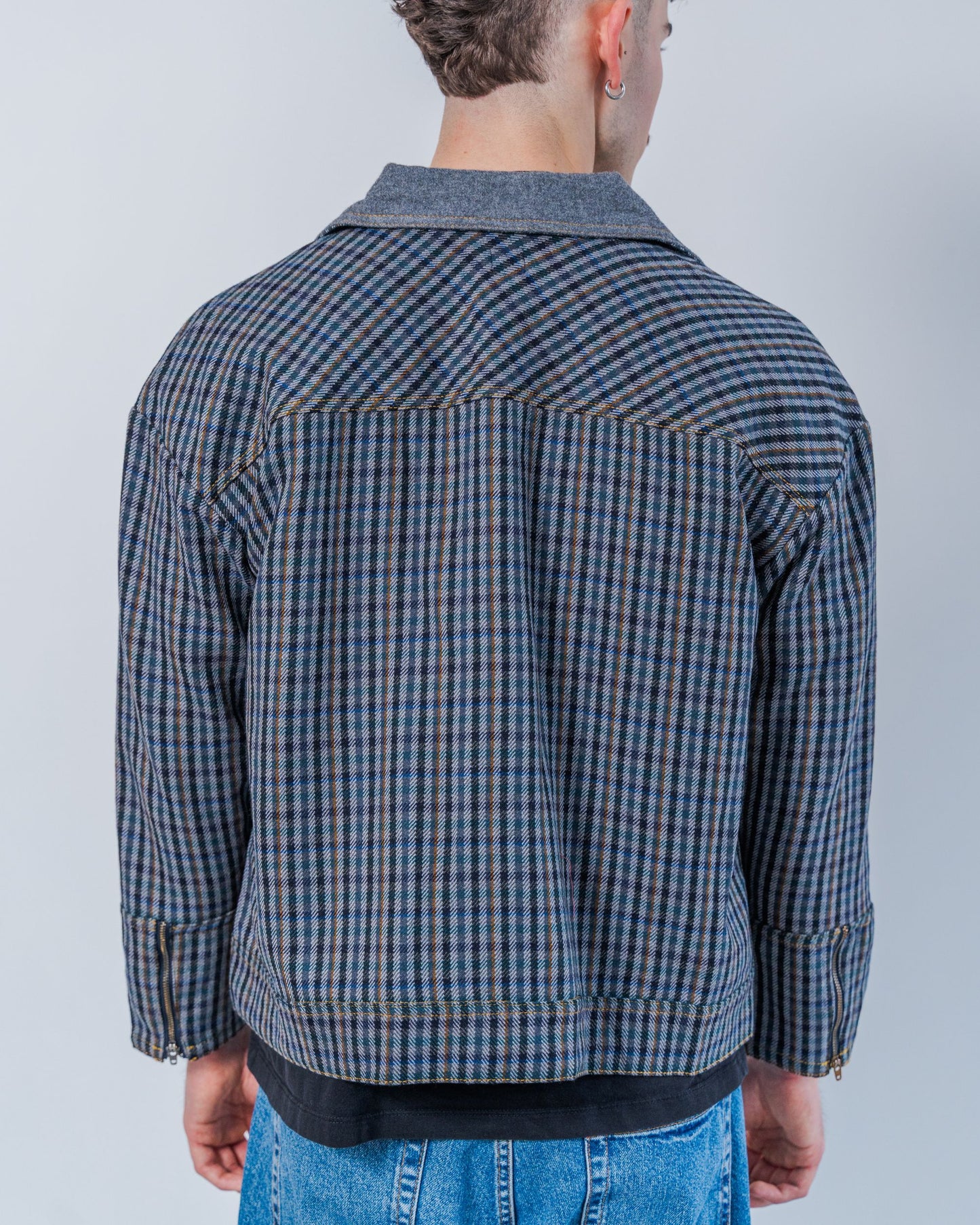 Man wearing a wool plaid jacket The jacket is sustainable and unisex, made from upcycled high quality wool materials. This photo shows the back of the jacket. 