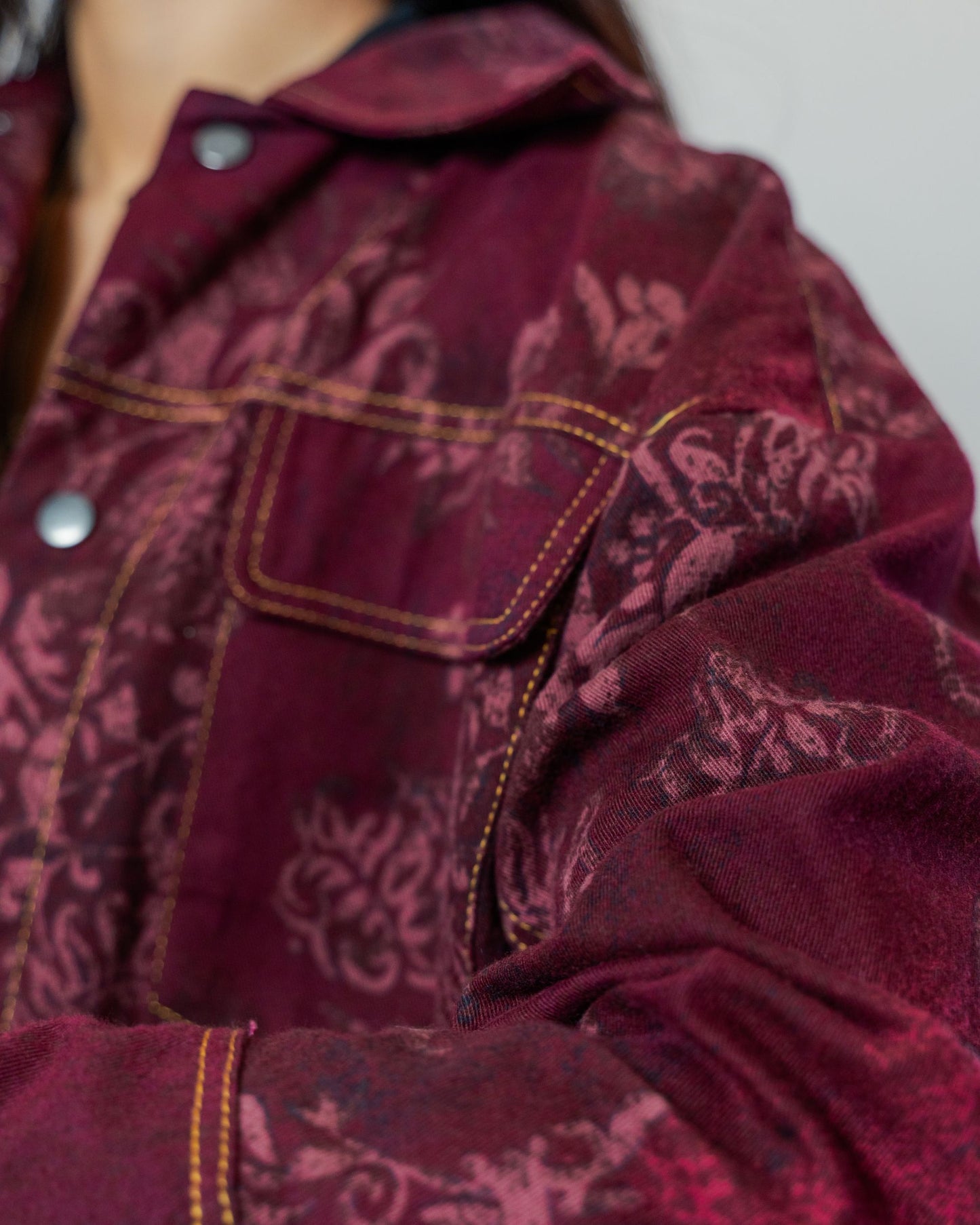 Close-up of a burgundy red patterned jacket gold top stitching made from sustainable upcycled materials.