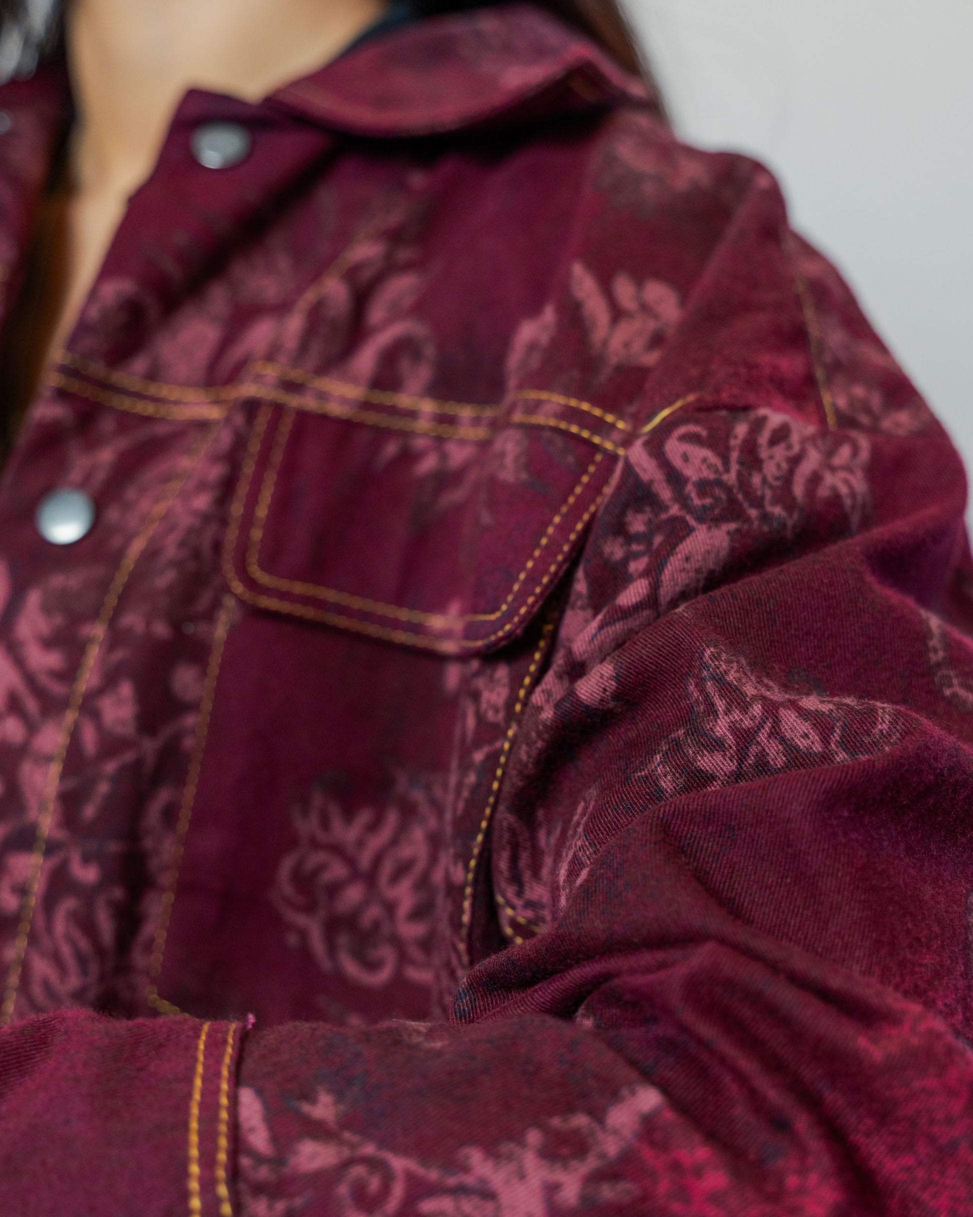 Close-up of a burgundy red patterned jacket gold top stitching made from sustainable upcycled materials.