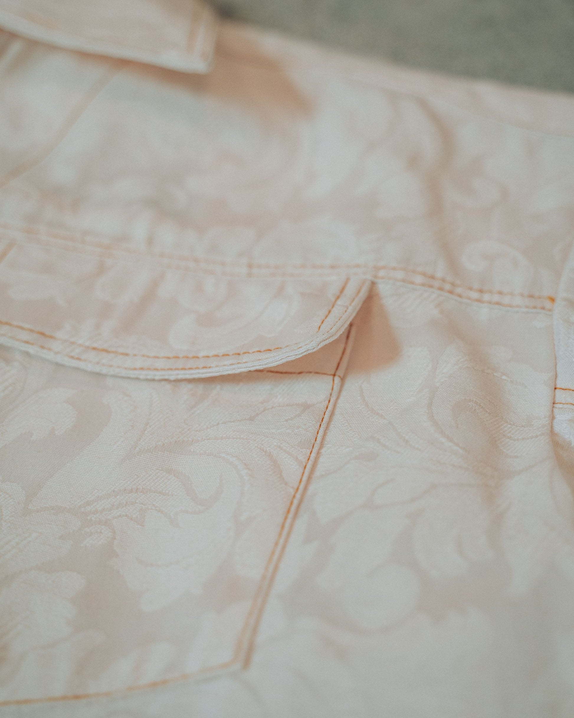 Close-up of a cream jacket pocket with top stitching on a blurred background