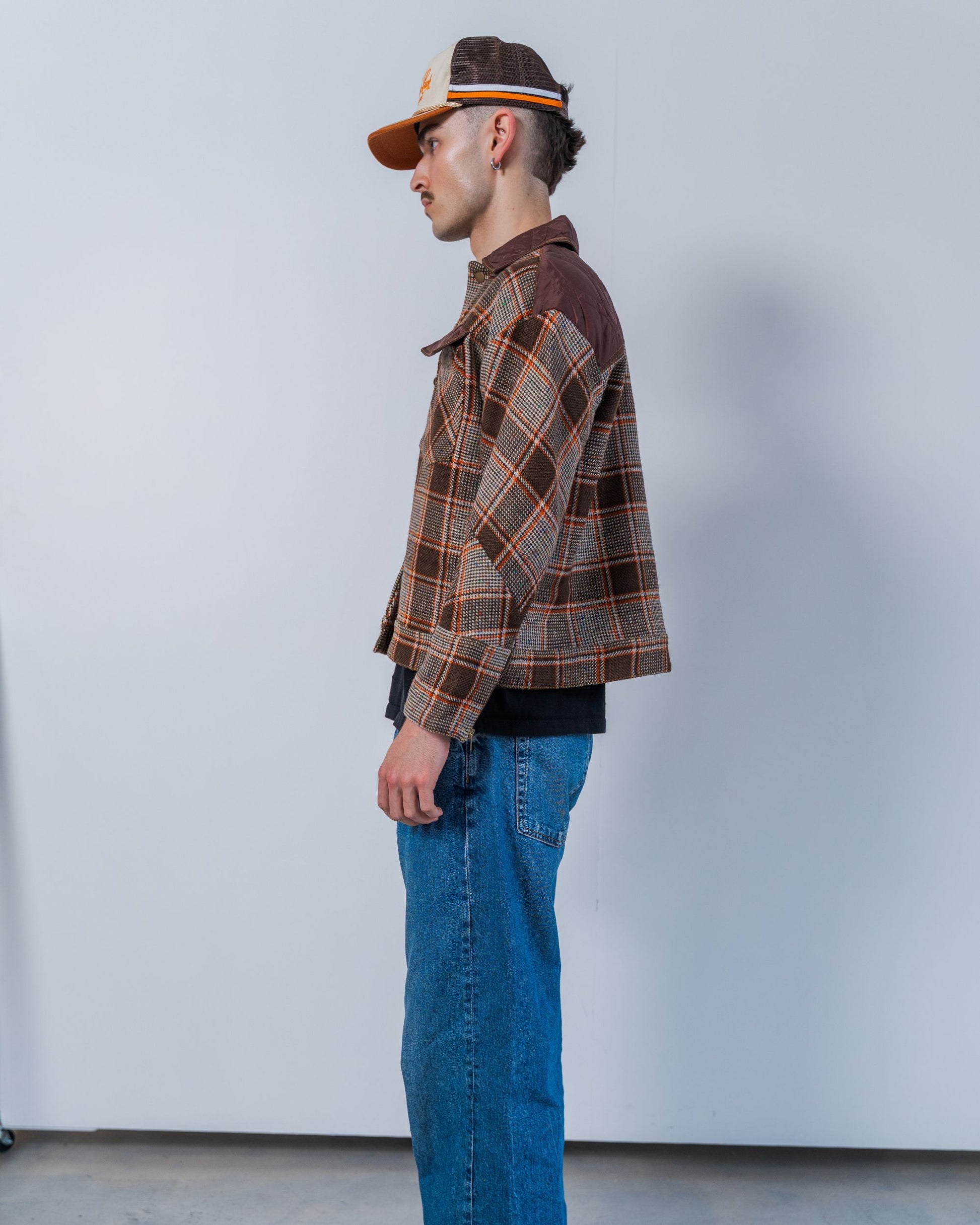 Man wearing a brown wool plaid jacket and blue jeans against a plain background. Unisex jacket made from sustainable upcycled materials. 