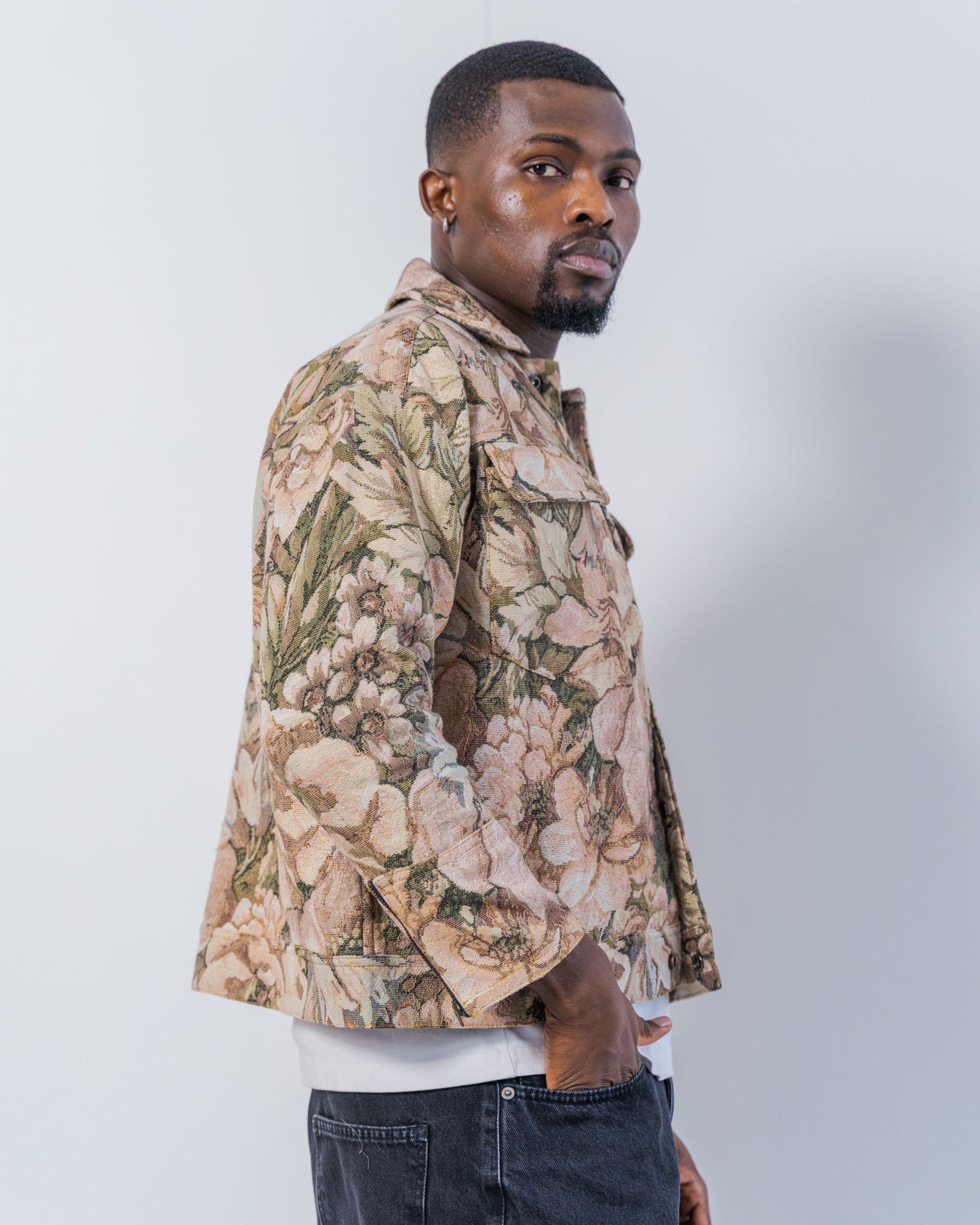 Man wearing a floral patterned jacket  made from upcycled materials on a plain background. The jacket is pink and brown with a jacquard floral print. It is sustainable and unisex. 