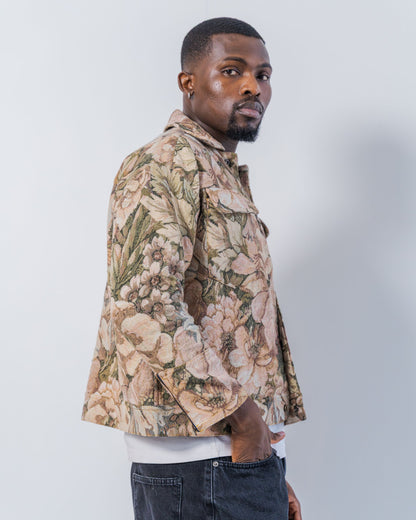 Man wearing a floral patterned jacket  made from upcycled materials on a plain background. The jacket is pink and brown with a jacquard floral print. It is sustainable and unisex. 