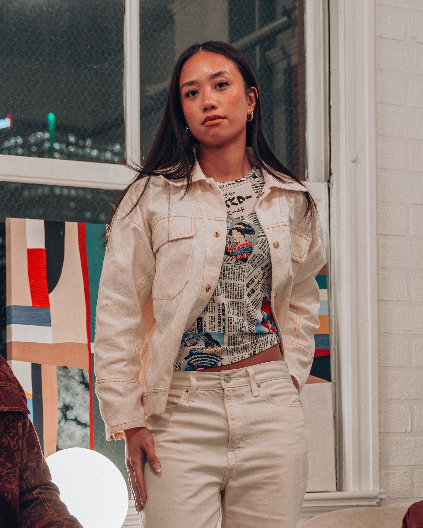 Woman wearing cream jacquard print jacket with gold buttons and top stitching styled with white pants and a printed shirt