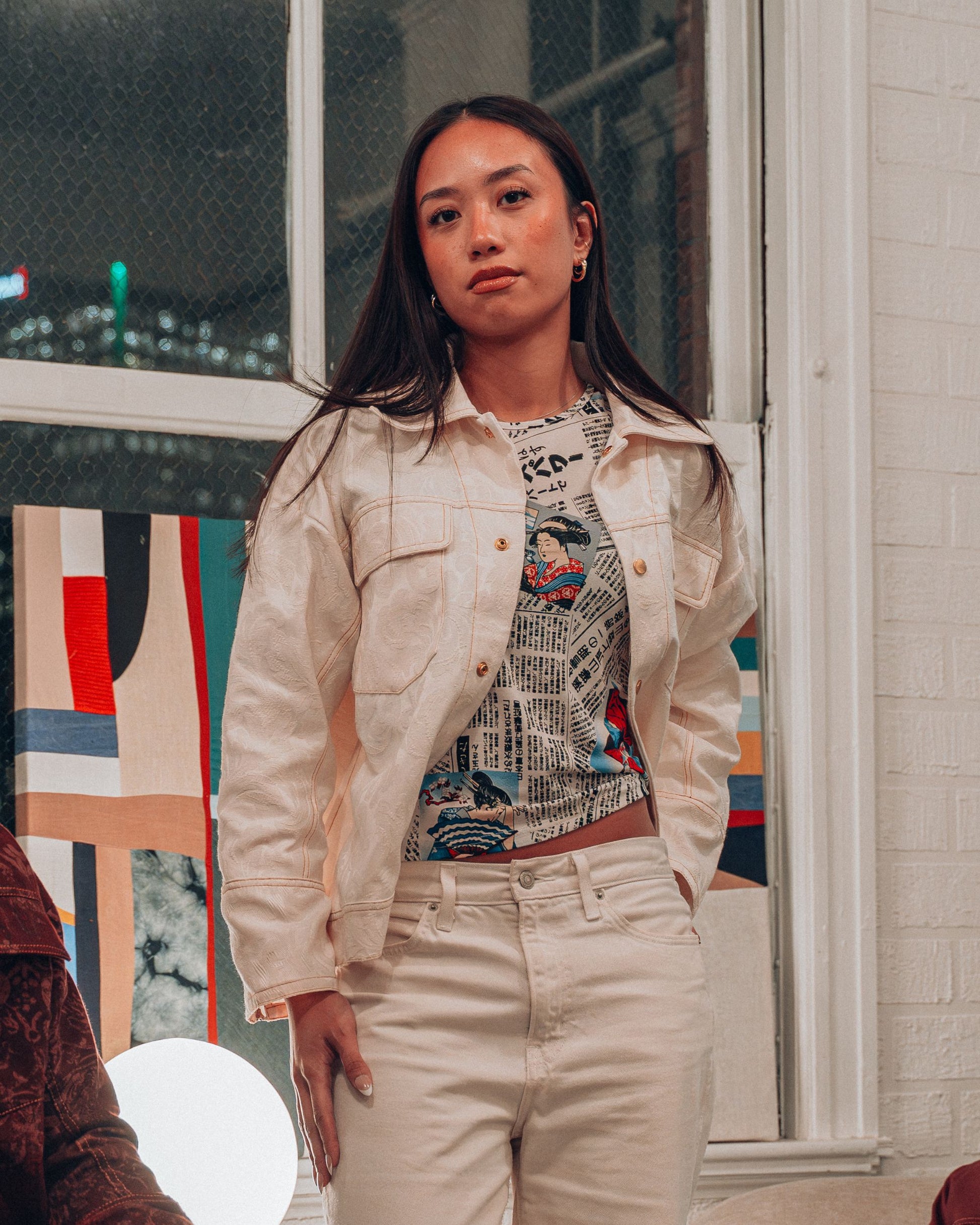 Woman wearing cream jacquard print jacket with gold buttons and top stitching styled with white pants and a printed shirt