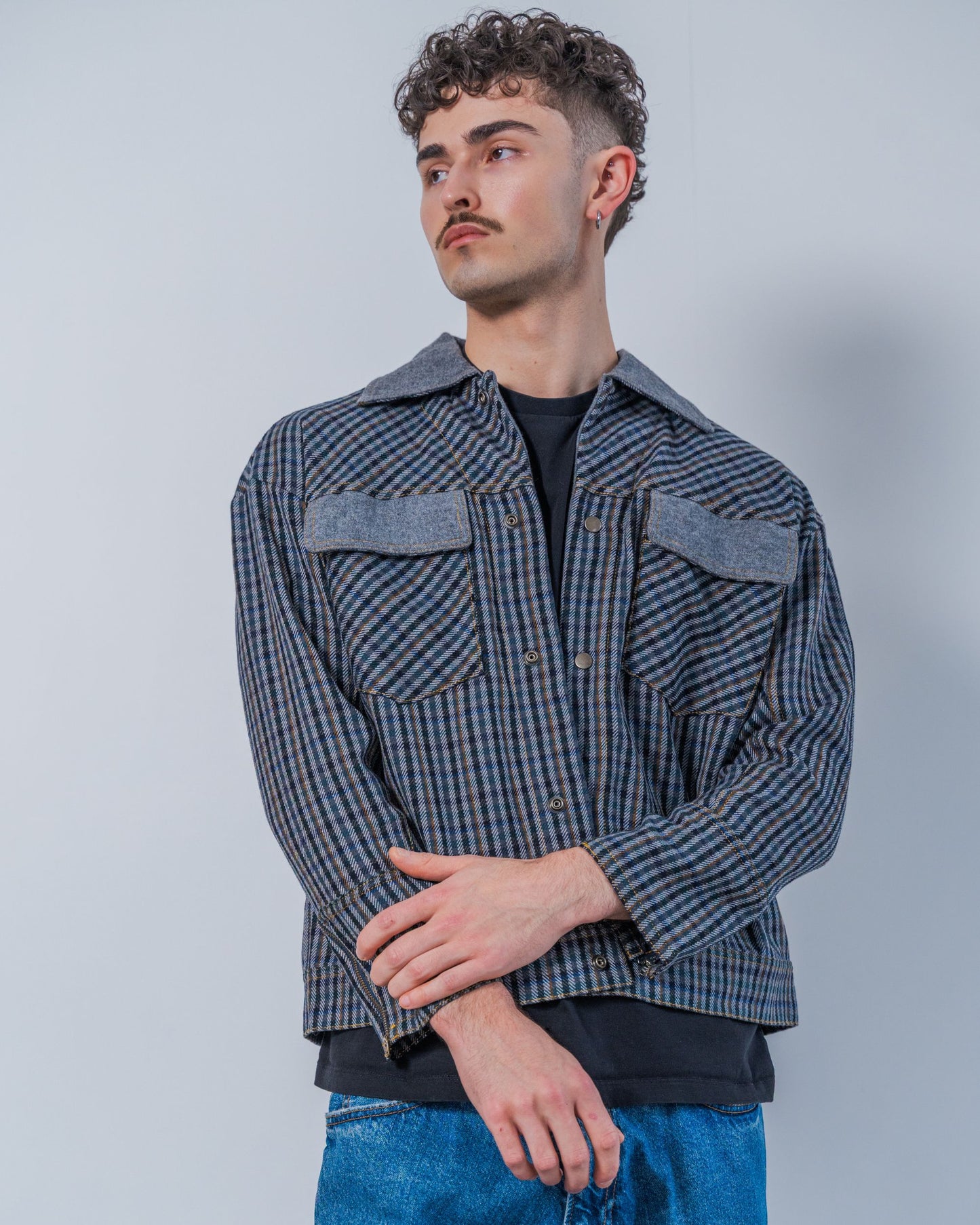 Man wearing a wool plaid jacket and jeans against a plain background. The jacket is sustainable and unisex, made from upcycled high quality wool materials.