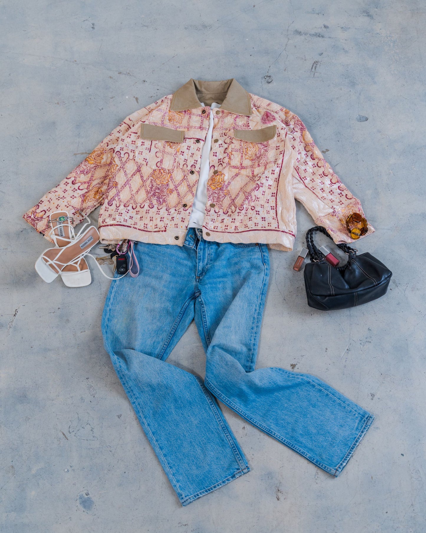 Flat lay styling of the sustainable unisex jacket with jeans, and accessories on a concrete floor. 